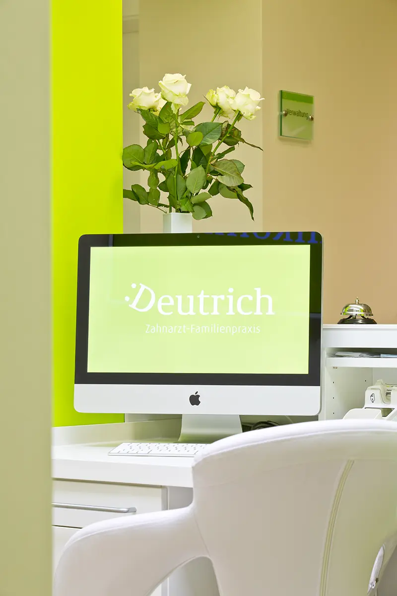 Blick hinter den aufgeräumten Empfangstresen der Zahnarztpraxis mit einem iMac-Computer.